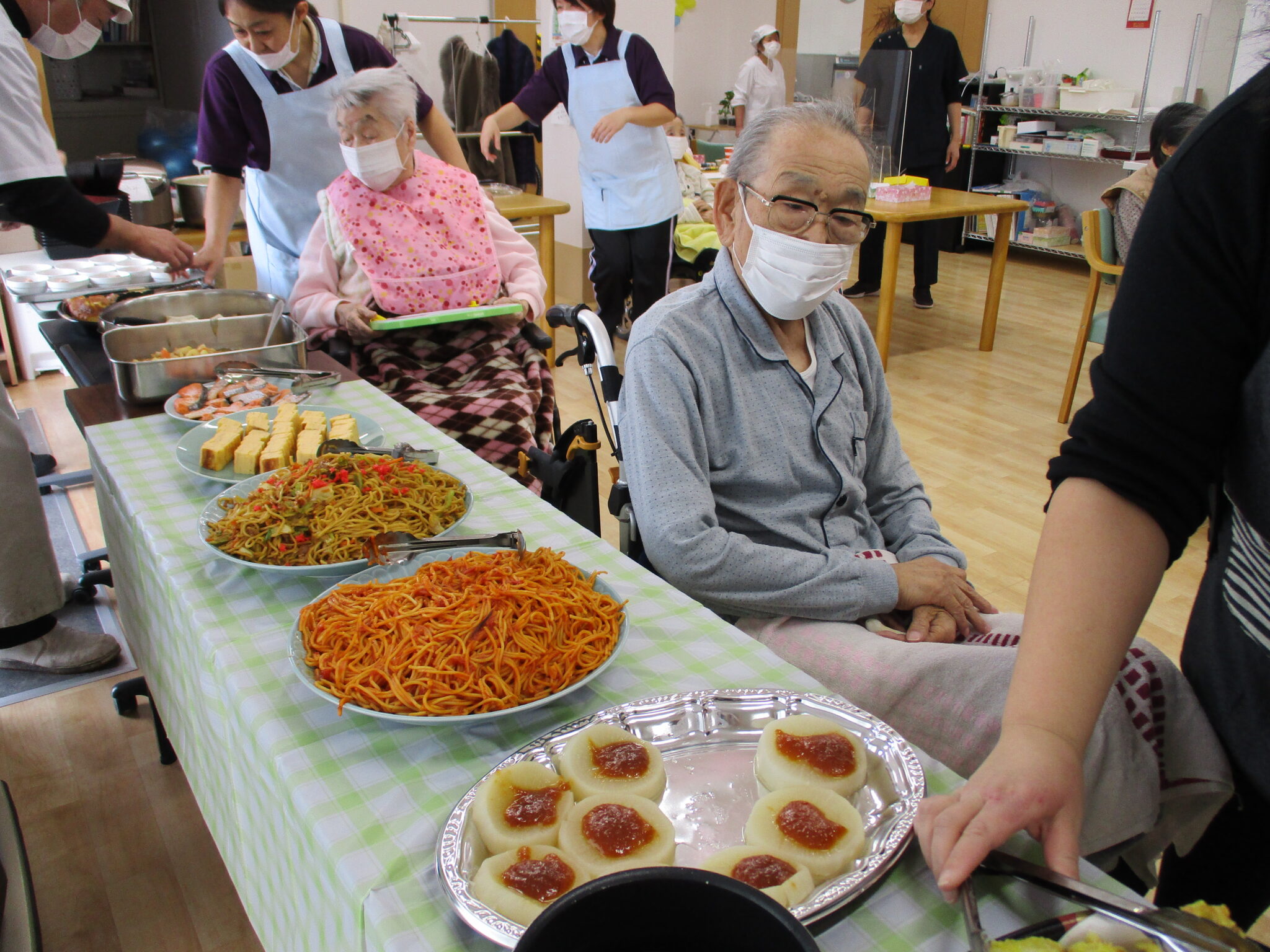 介護施設で入居者とスタッフが一緒に食事をしながら楽しむ風景。